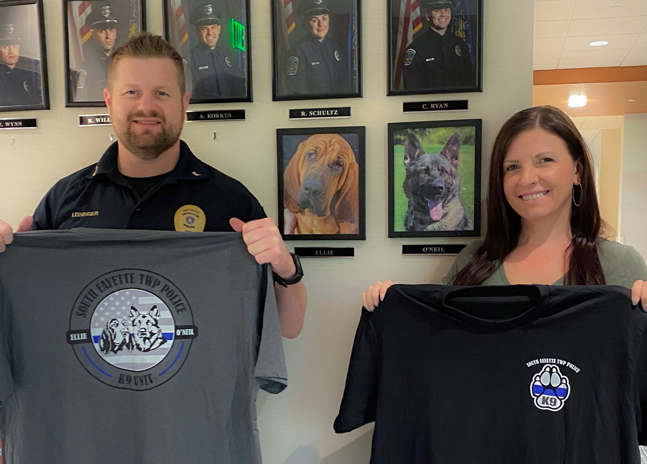 Two people holding K9 shirts with dog photos on wall