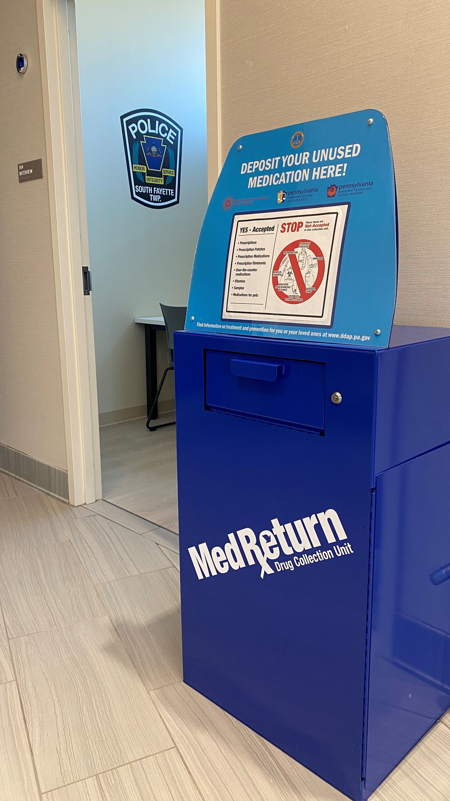 Blue medication dropbox with open door and police patch in background